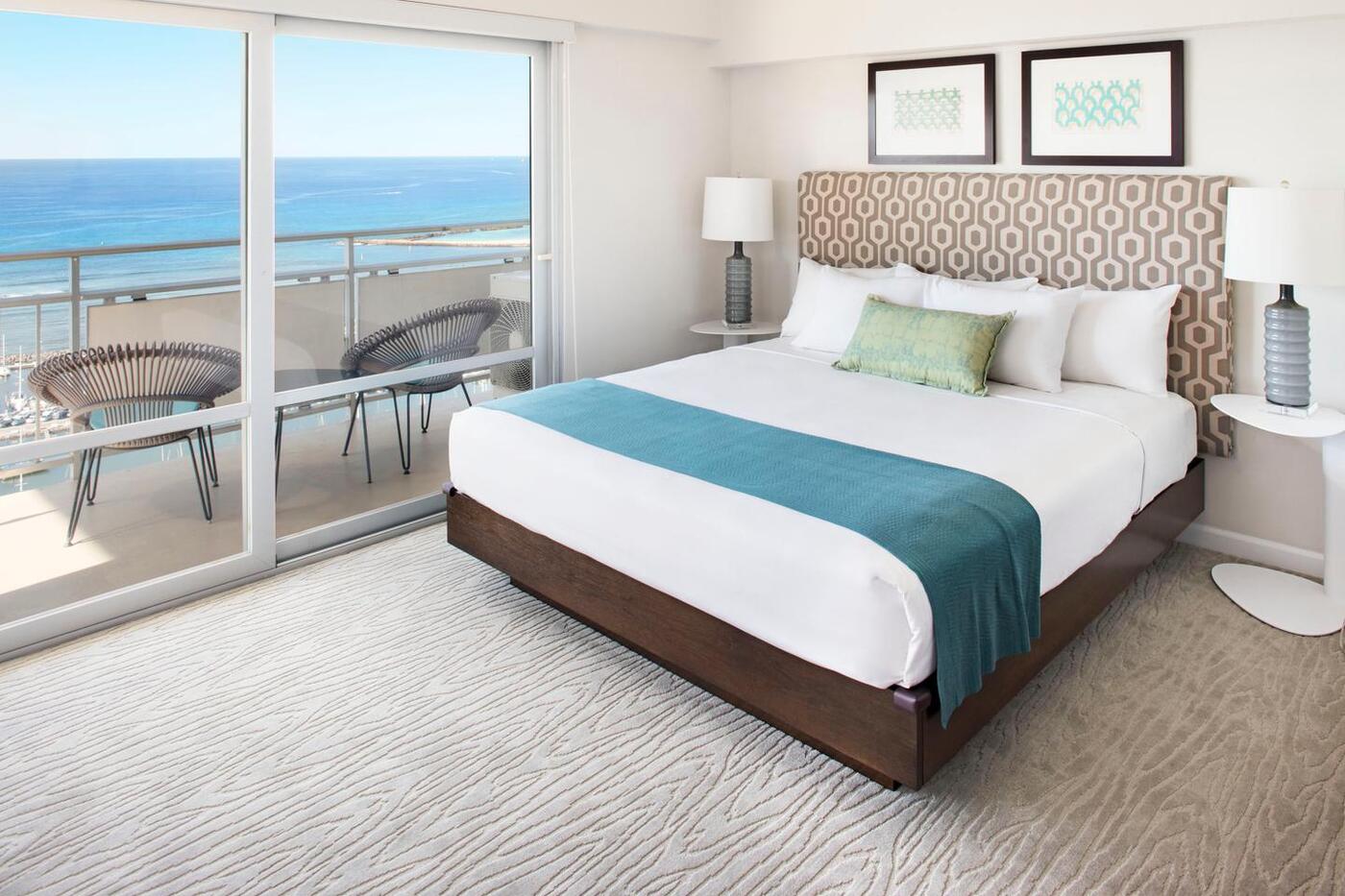 Room with bed, nightstands, lamps, and balcony with ocean views.