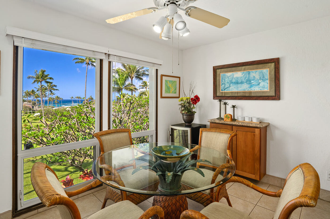 Dining area with table, chairs, balcony with garden and ocean views in distance.